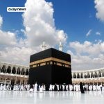 Pilgrims gathered around the Kaaba at Masjid al-Haram in Mecca under a bright blue sky with scattered clouds.